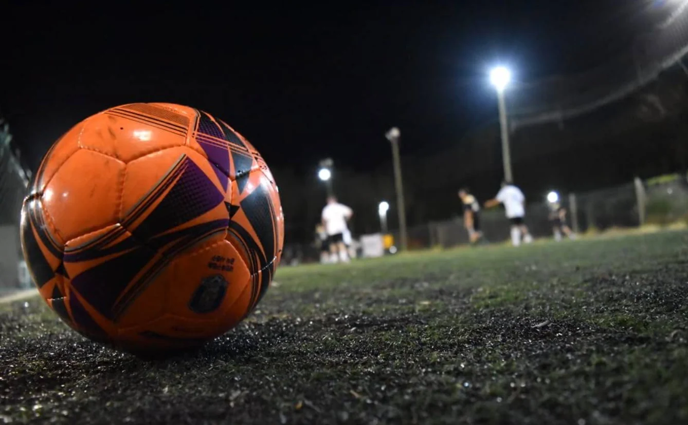 Pelota de fútbol sobre el césped durante un partido nocturno en Rústico 6